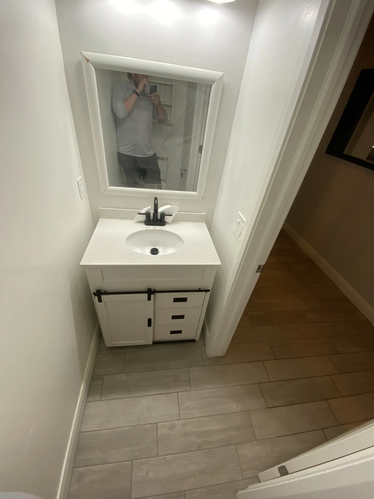Finished bathroom with new tile floor — white vanity with black hardware and new plank tile