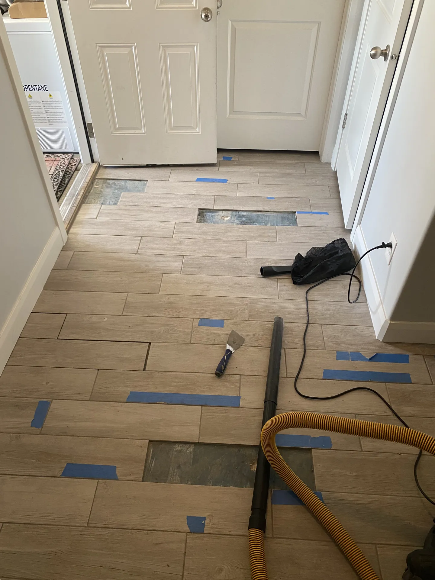 Tile installation progress — wood-look plank tile mostly laid in entryway with blue tape spacers