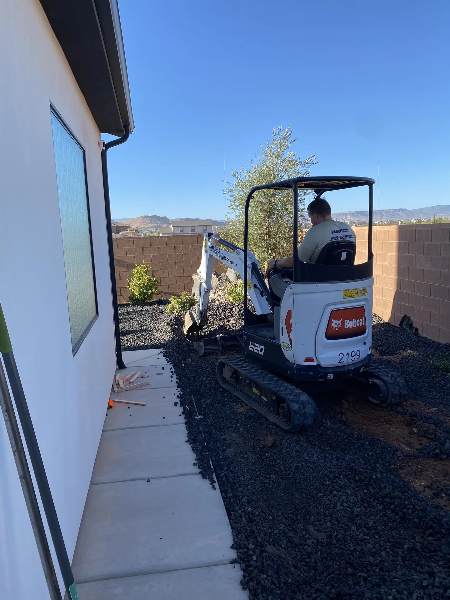 Bobcat excavator digging the shed site through rocky soil with mountains behind
