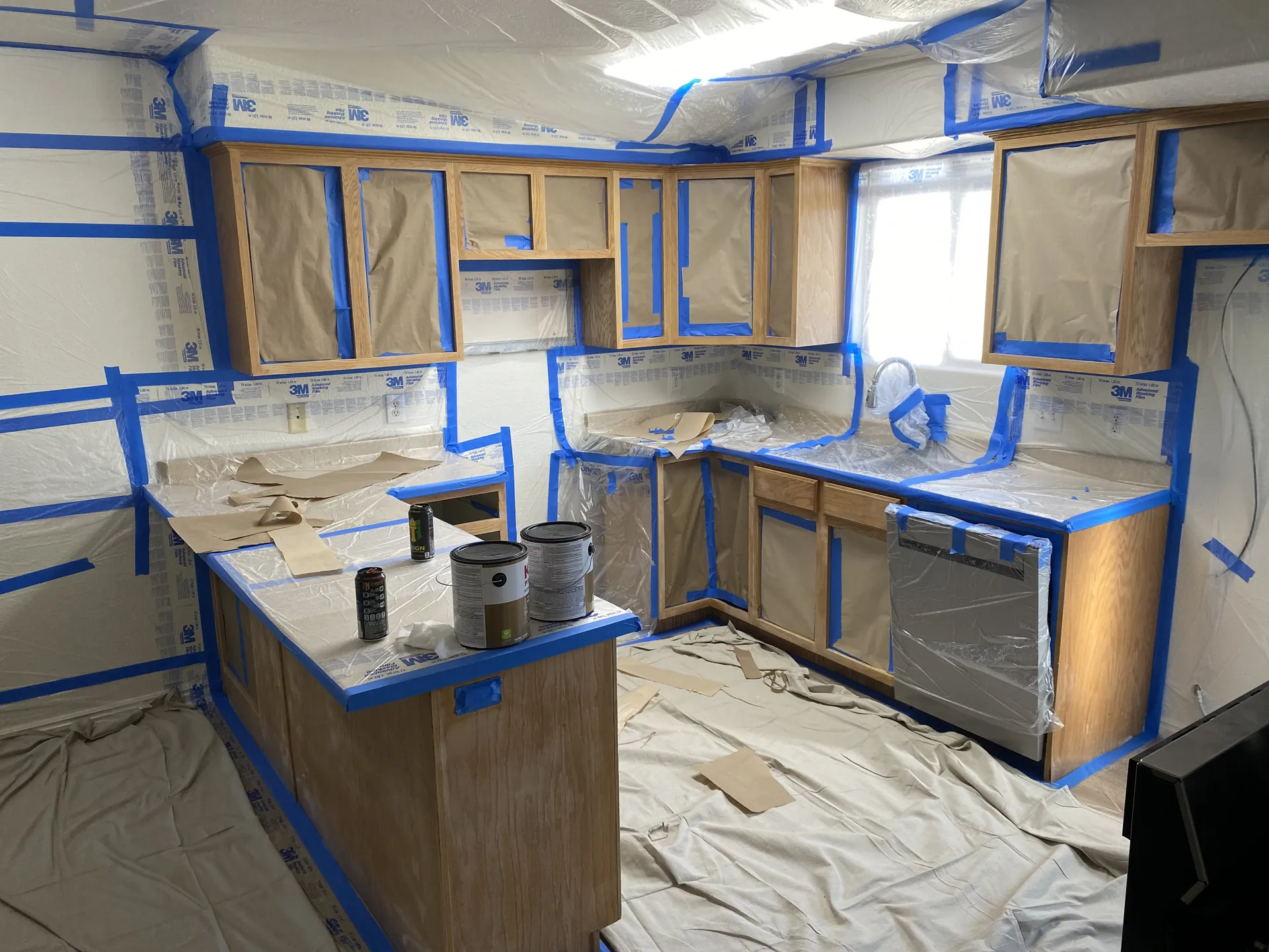 Second view of the masked kitchen during the cabinet painting phase