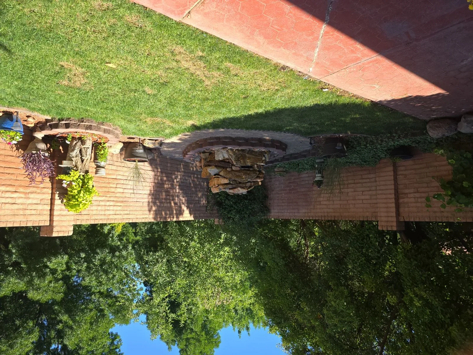 Wide backyard view of the finished fountain in context with the paver walkway, lawn, and mature trees