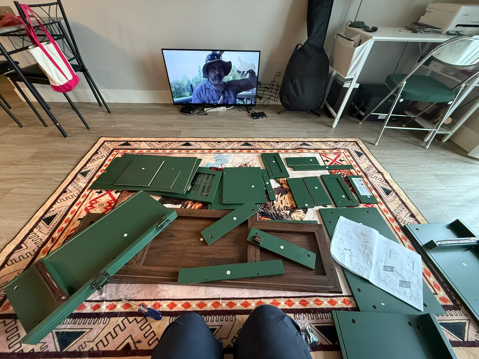 Flat-pack TV console panels and hardware laid out on a living room rug with the instruction sheet before assembly