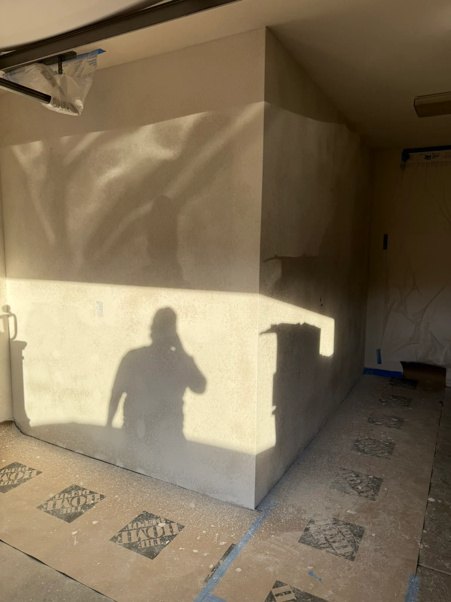 Finished spray-textured corner of the garage storage room with masking film still protecting the nearby door