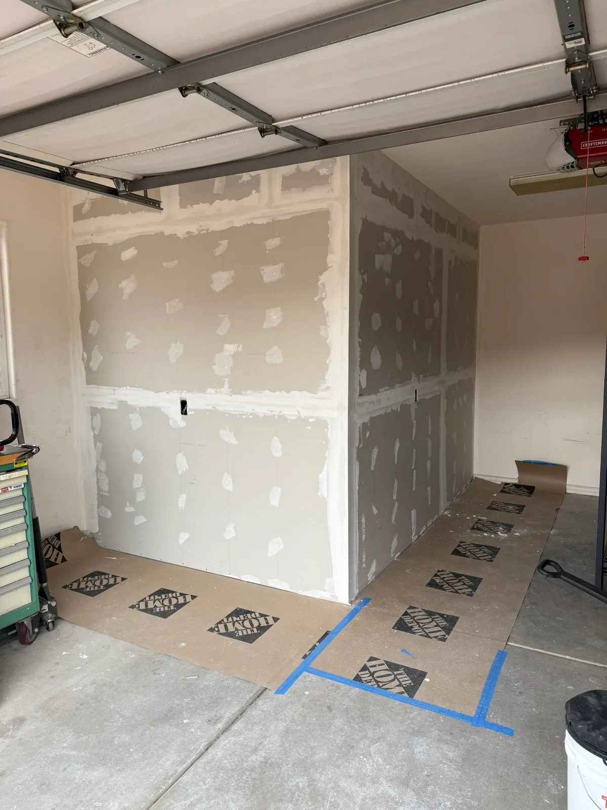 Drywall seams taped and first mud coat applied on a garage storage room, screw heads spotted