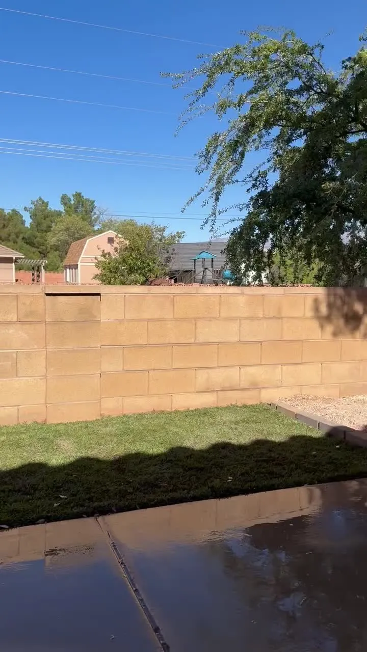Finished new sod lawn being watered in beside a concrete patio and block wall in Santa Clara, Utah