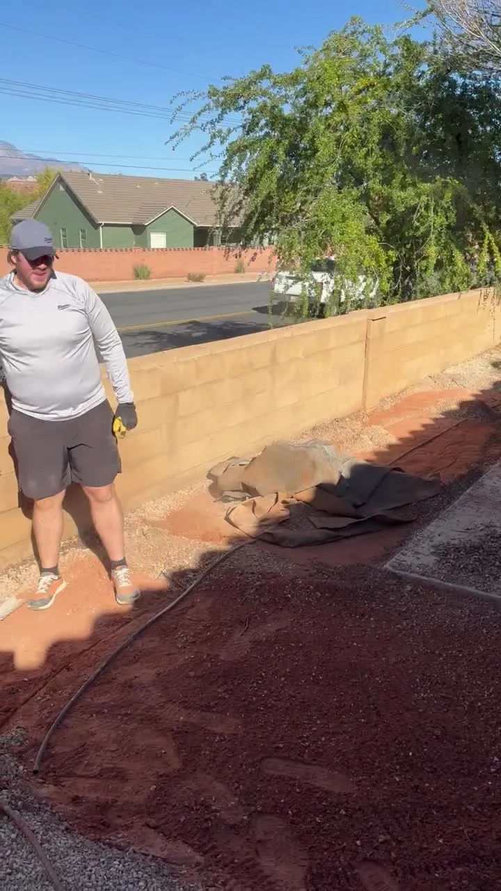 Dark topsoil spread over native red dirt and raked toward the block wall during sod ground preparation