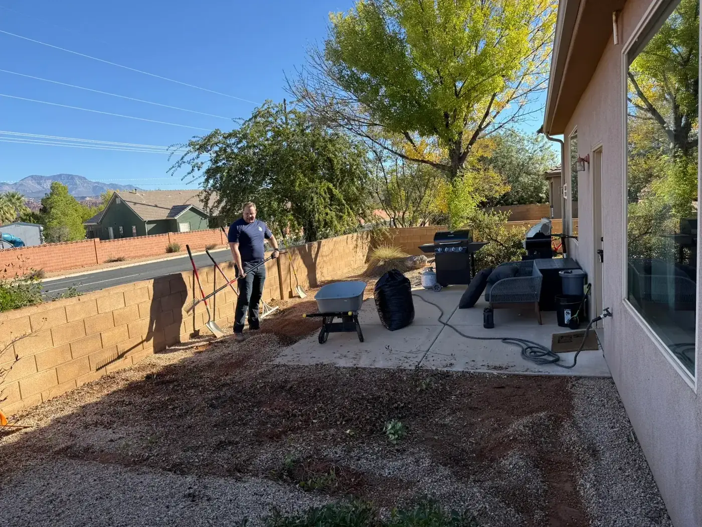 Viking Solutions crew member raking and clearing a bare dirt backyard beside a concrete patio in Santa Clara, Utah before sod installation
